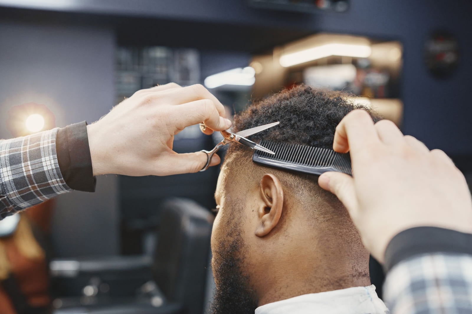 Un barbero de pie terminando el corte de un cliente sentado en la silla.