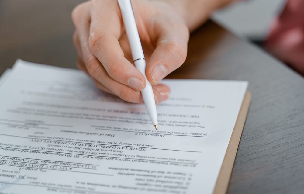 A hand signing the last page of a printed document with a plain white pen.