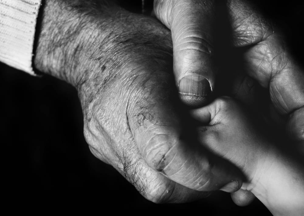A young hand resting in the open hand of an older person, photographed in black and white.