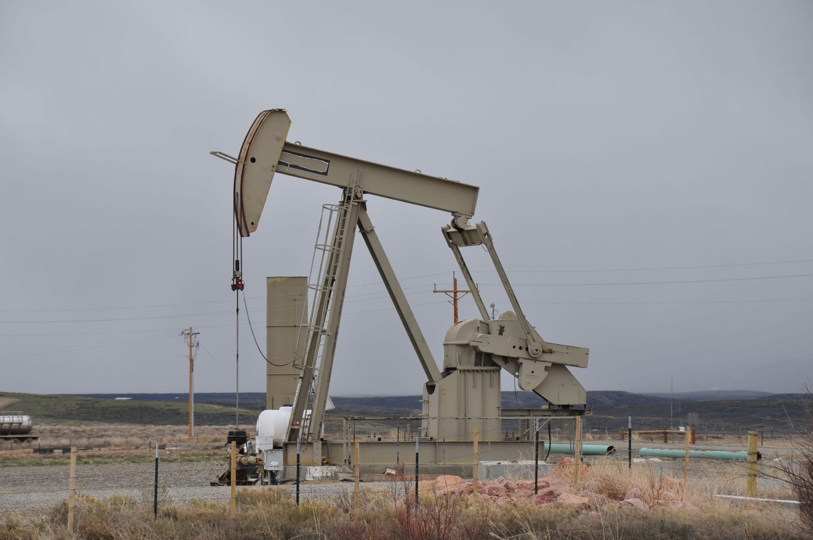 A wellhead on a West Texas lease: stacked valves and flanges in chipped red paint with pressure gauges, and a rod pump jack standing behind it.