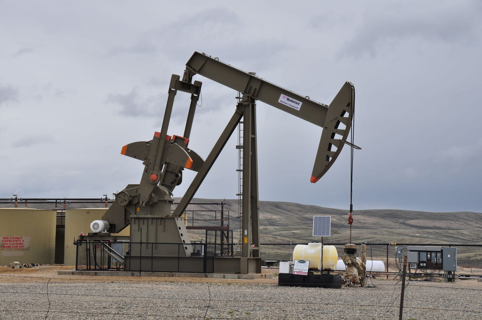 A pump jack and associated wellhead equipment at a remote lease site under a cloudy sky.