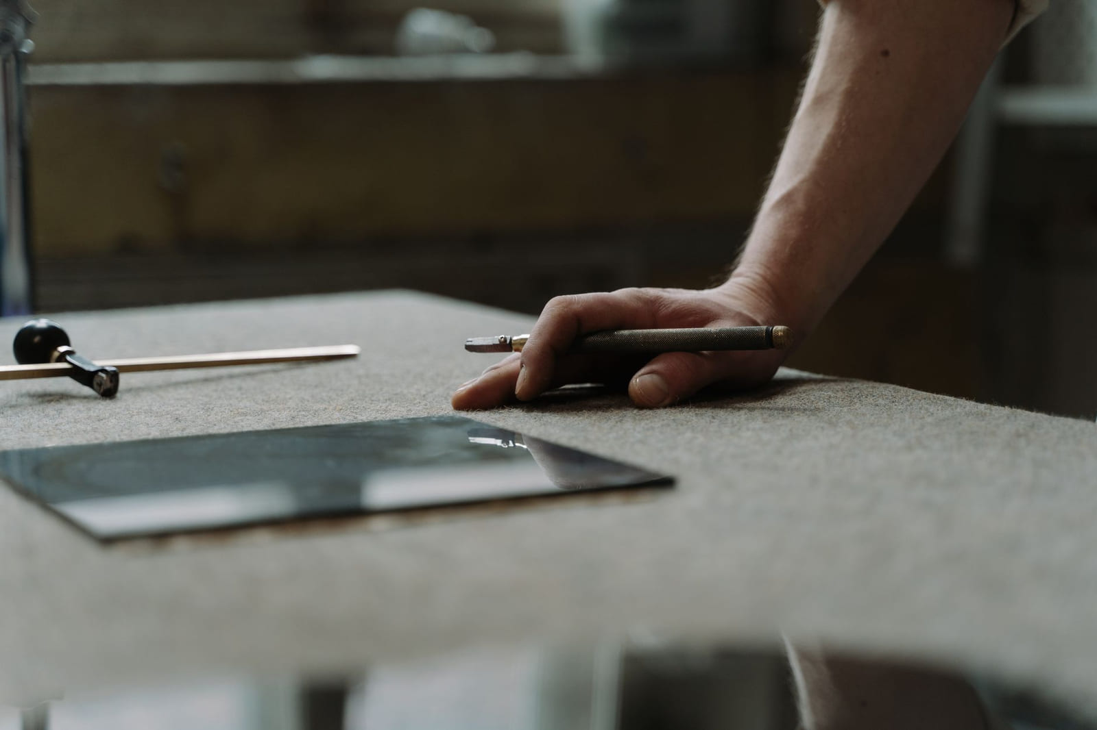Hands working a sheet of glass flat on a felt-covered cutting table.