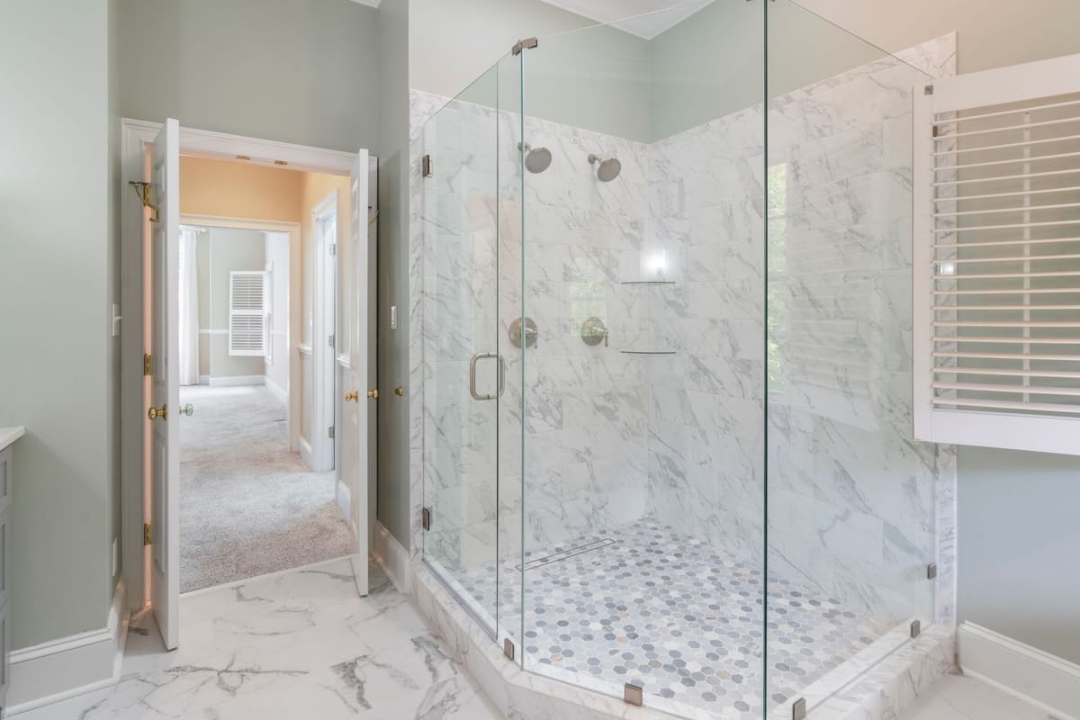 A finished primary bathroom with a curbless glass shower, marble slab walls and a pebble mosaic floor.