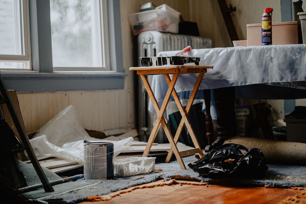 A room stripped for work: drop cloths on the subfloor, a folding table under plastic sheeting, a paint can and tray.