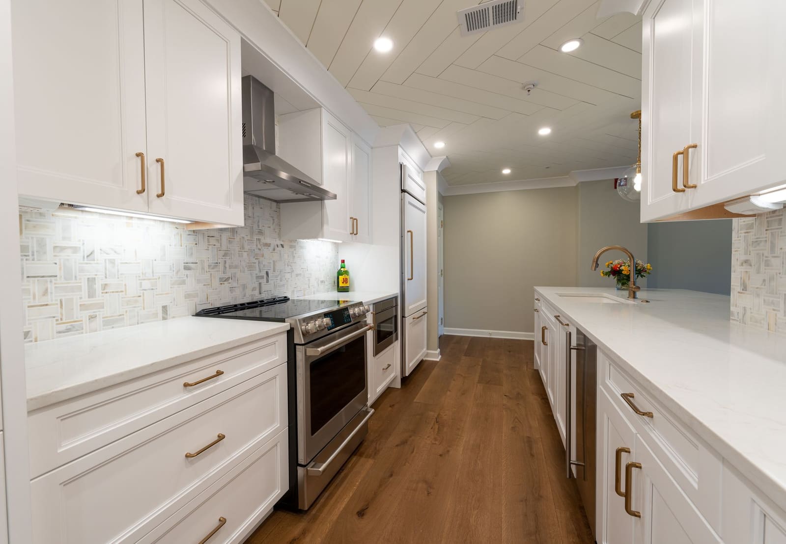 A finished galley kitchen in Bellaire: white shaker cabinets, brass pulls, marble counters and a mosaic backsplash.